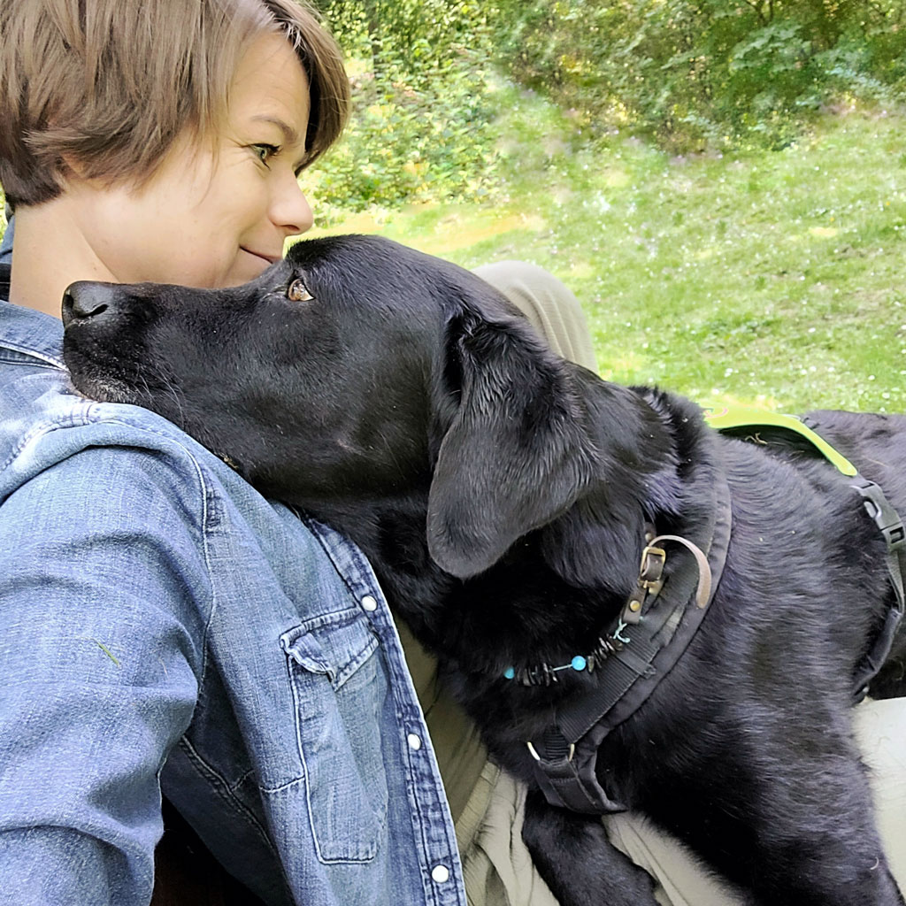 Frau mit braunem Haar und Lächeln mit schwarzem Labrador im grünen Park.